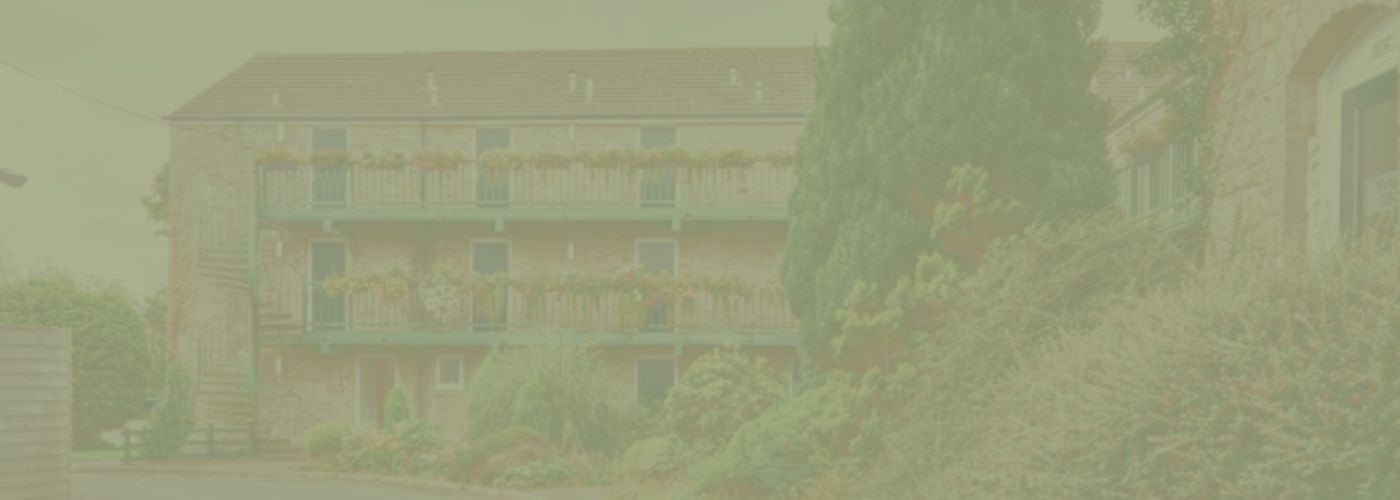 External view of a building at the Melbreak hotel, with flowers lining the balconies with a green background